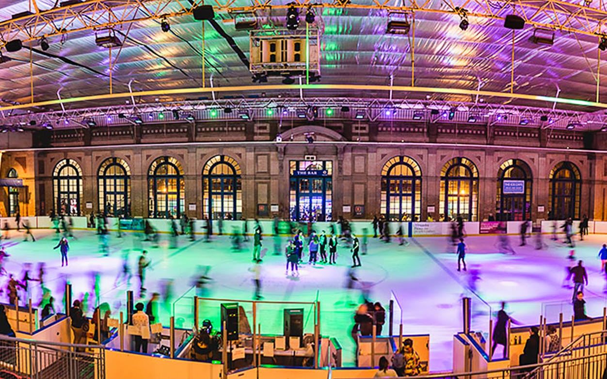 Ice skaters enjoying Alexandra Palace Ice Rink in London under colorful lights.