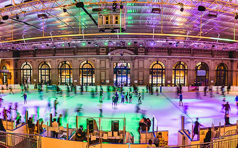 Ice skaters enjoying Alexandra Palace Ice Rink in London under colorful lights.