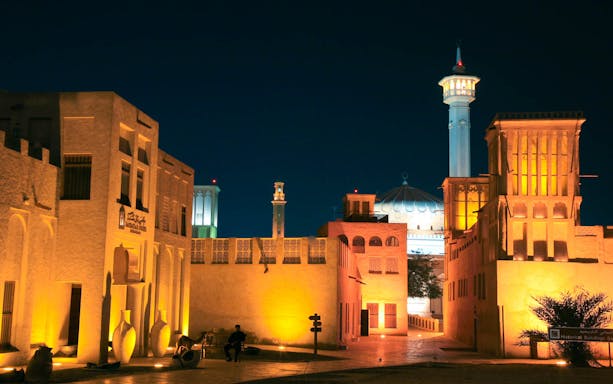 Historic Al Fahidi neighborhood in Dubai at night, featuring traditional wind towers and illuminated mosque.