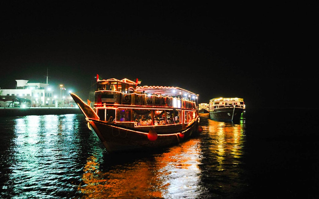 Dhow boats illuminated at night on Dubai Creek during a dinner cruise.