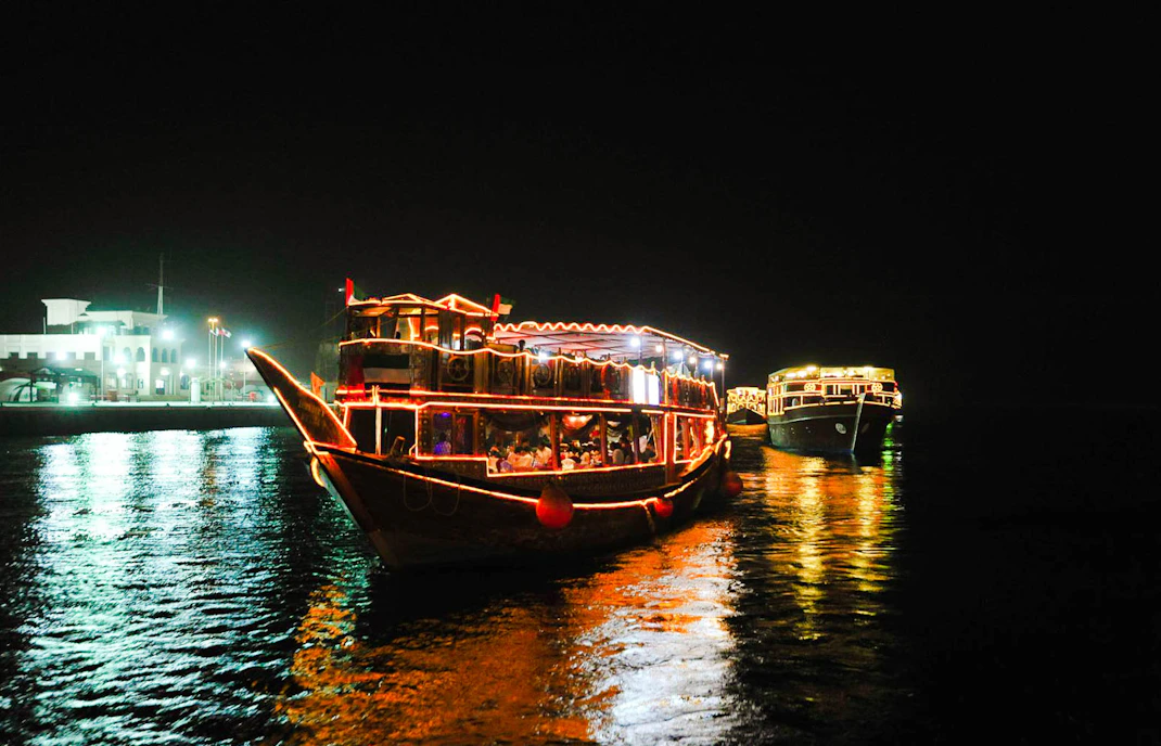 Dhow boats illuminated at night on Dubai Creek during a dinner cruise.