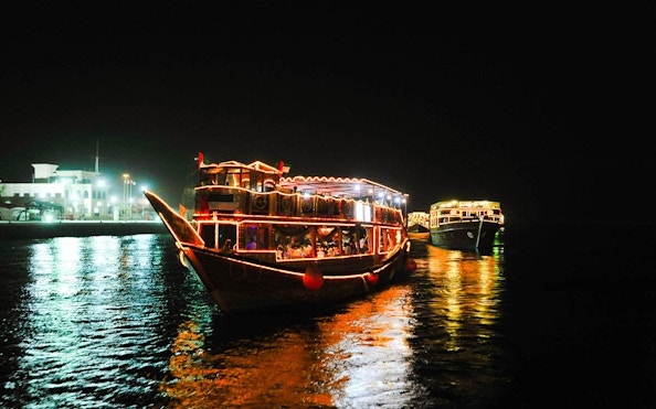 Dhow boats illuminated at night on Dubai Creek during a dinner cruise.