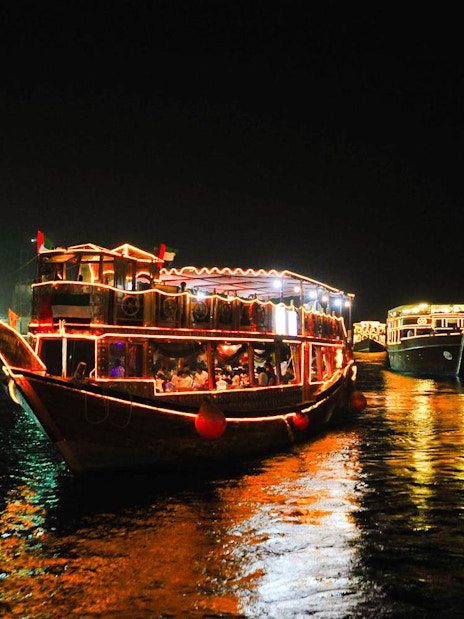 Dhow boats illuminated at night on Dubai Creek during a dinner cruise.