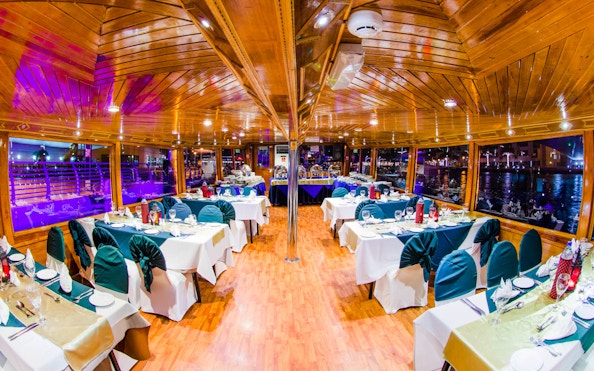 Dhow dinner cruise interior with set tables on Dubai Creek.