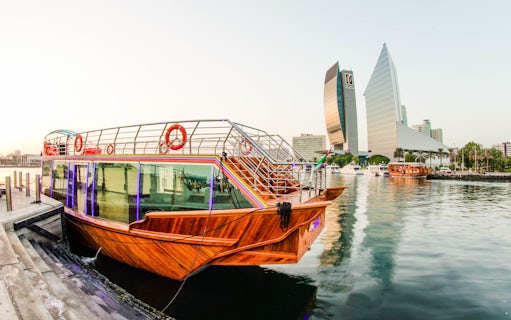 Dhow boat docked on Dubai Creek with city skyline in the background.