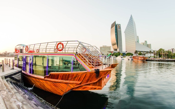 Dhow boat docked on Dubai Creek with city skyline in the background.