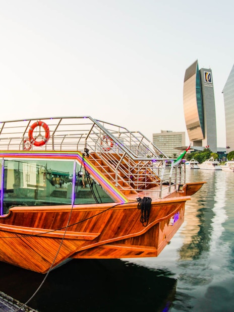 Dhow boat docked on Dubai Creek with city skyline in the background.