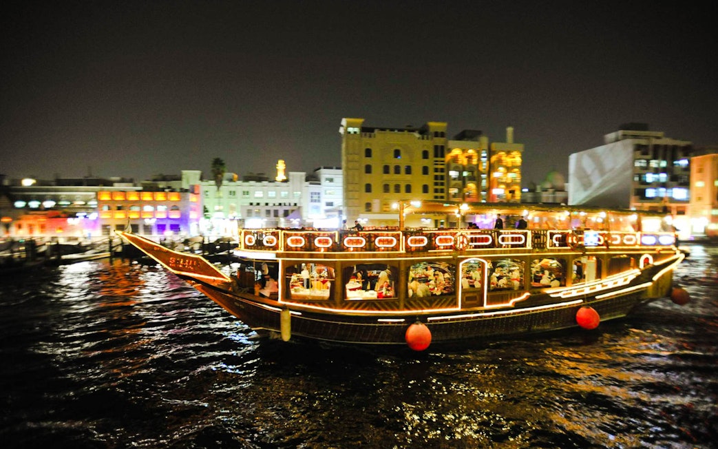 Dhow boat illuminated at night on Dubai Creek during dinner cruise.