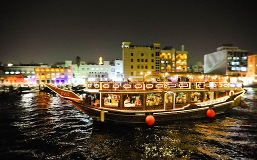 Dhow boat illuminated at night on Dubai Creek during dinner cruise.