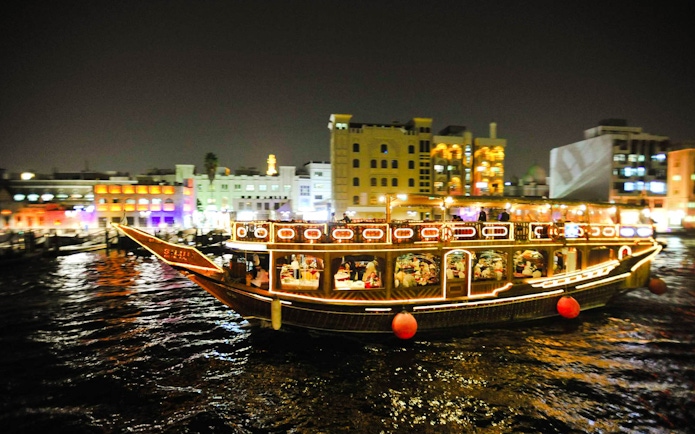 Dhow boat illuminated at night on Dubai Creek during dinner cruise.