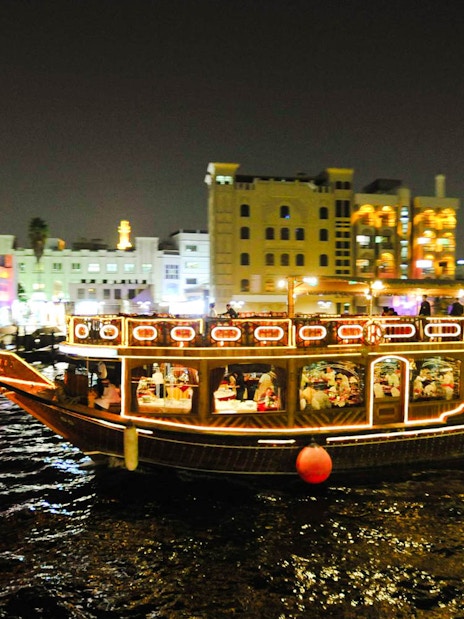 Dhow boat illuminated at night on Dubai Creek during dinner cruise.