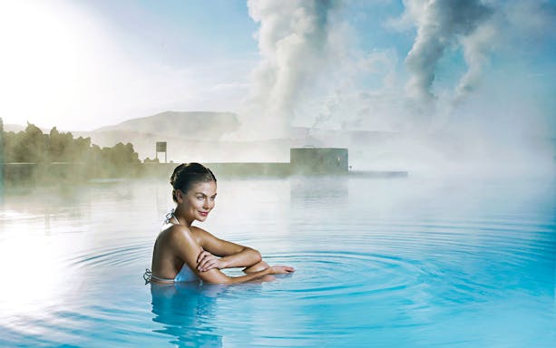 Person relaxing in the geothermal waters of Blue Lagoon, Iceland, with steam rising in the background.