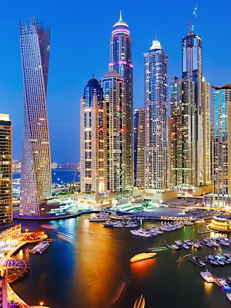 Dubai Marina skyline at night with illuminated skyscrapers and yachts, Combo: Dhow Cruise + Desert Safari.