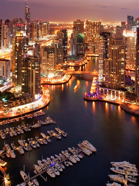 Dubai Marina skyline at night with illuminated skyscrapers and yachts, part of Dhow Cruise + Desert Safari combo.