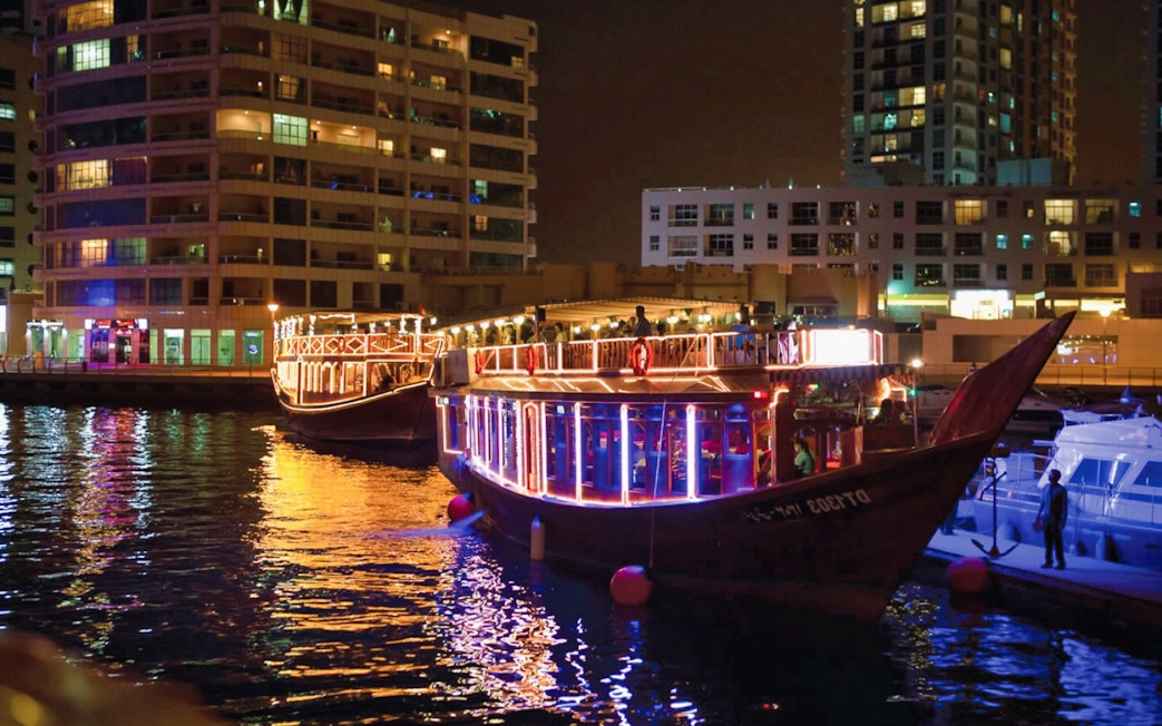 Dhow boats illuminated at night in Dubai Marina during a dinner cruise with live entertainment.