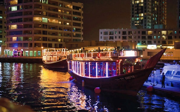 Dhow boats illuminated at night in Dubai Marina during a dinner cruise with live entertainment.