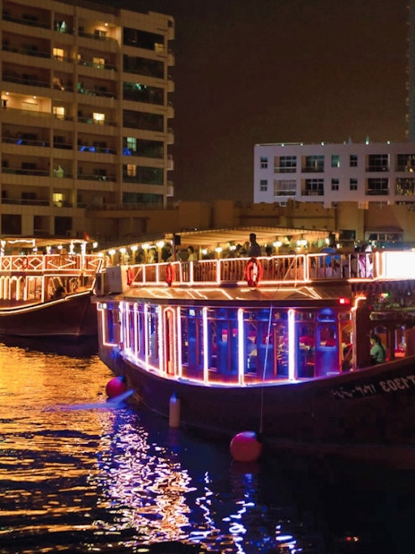 Dhow boats illuminated at night in Dubai Marina during a dinner cruise with live entertainment.