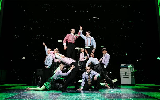 Performers on stage in a scene from "The Wedding Singer" musical, with money flying around.