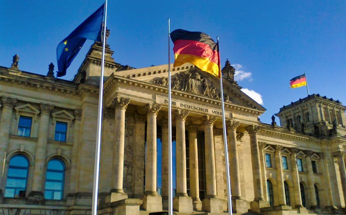 Reichstag building in Berlin with German and EU flags flying.