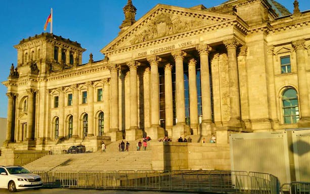 Reichstag building in Berlin with visitors on the steps, German flag flying.