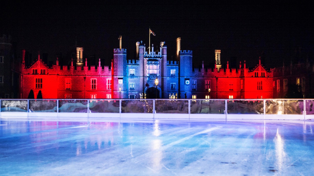 Hampton Court Palace illuminated at night behind ice rink in London.