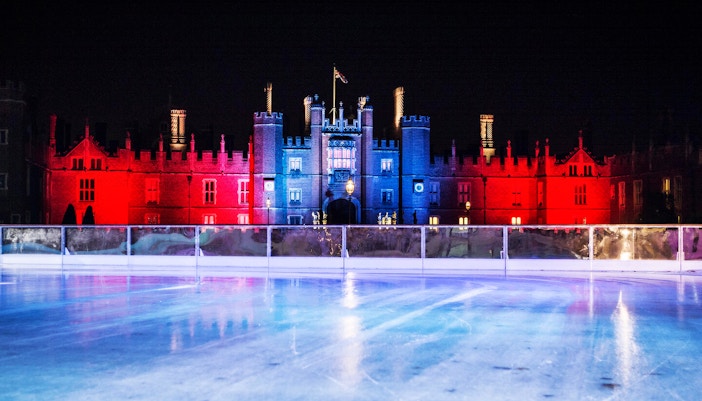 Hampton Court Palace illuminated at night behind ice rink in London.