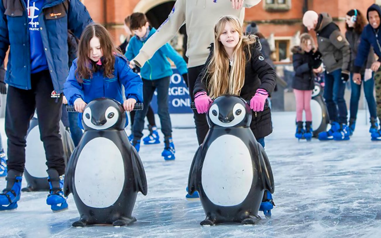 Children ice skating with penguin aids at Hampton Court Palace rink, London.