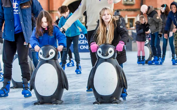 Children ice skating with penguin aids at Hampton Court Palace rink, London.