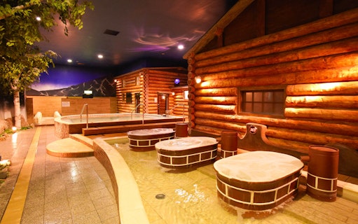 Indoor hot spring area with wooden log cabin decor at Spa World Osaka.