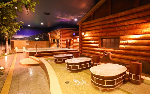 Indoor hot spring area with wooden log cabin decor at Spa World Osaka.
