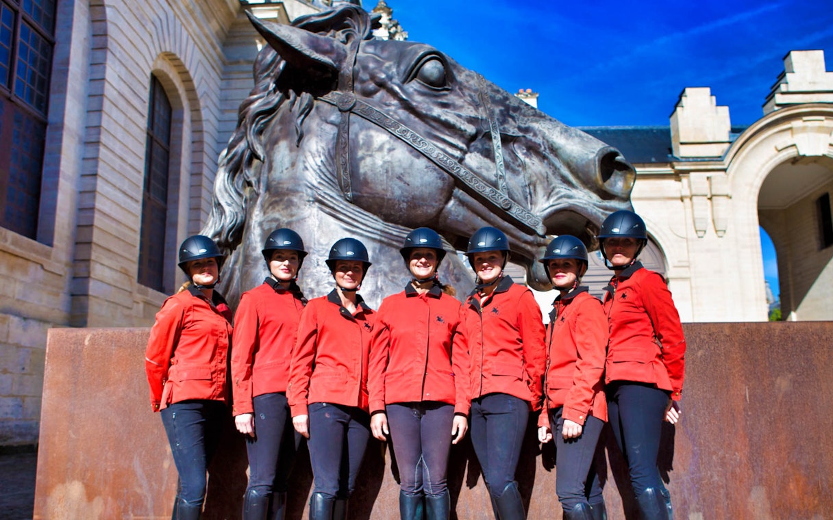 Equestrian team in red jackets at Chateau of Chantilly statue.