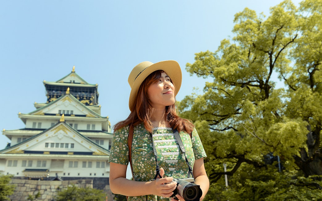 Tourist with camera in front of Osaka Castle, Japan, using Osaka Amazing Pass.