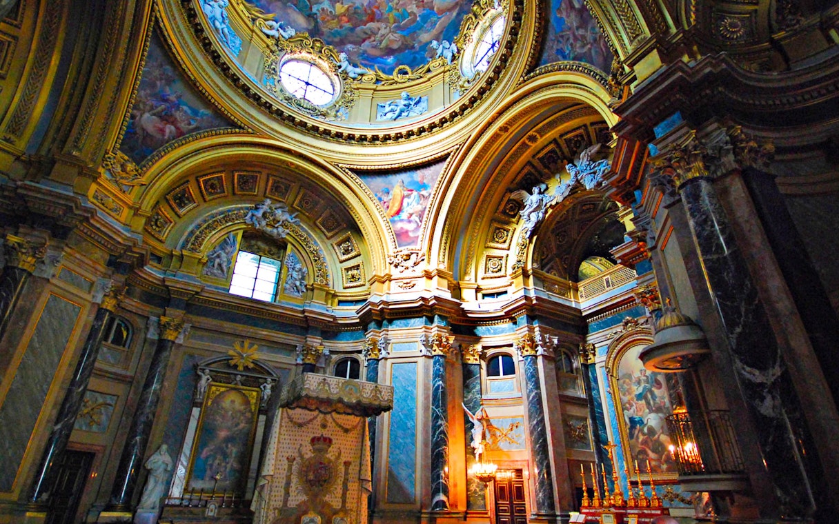 Royal Palace interior with ornate ceiling and columns, featuring detailed frescoes and gold accents.