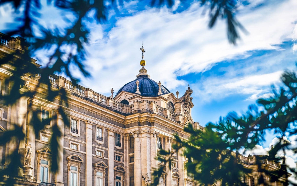 Royal Palace facade with dome, Madrid, viewed through tree branches.