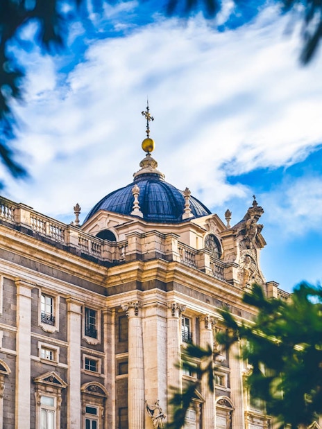 Royal Palace facade with dome, Madrid, viewed through tree branches.