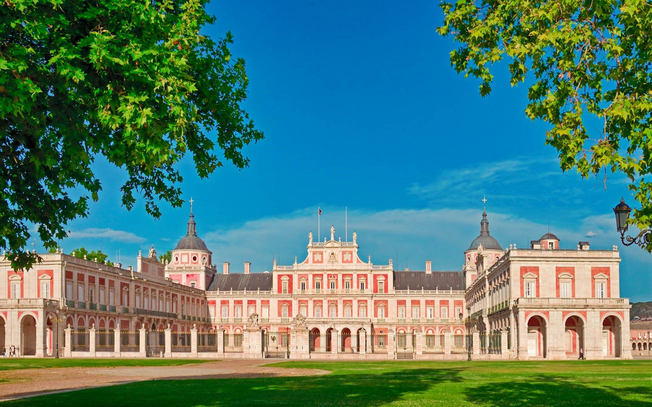 Royal Palace of Aranjuez facade with clear blue sky and green trees.