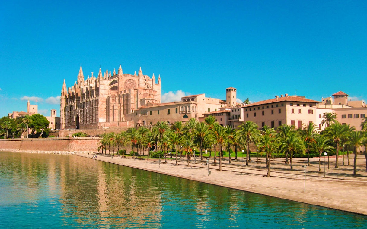 Royal Palace of La Almudaina with palm trees and waterfront in Palma, Mallorca.