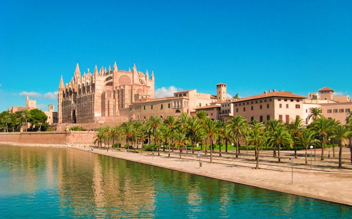Royal Palace of La Almudaina with palm trees and waterfront in Palma, Mallorca.