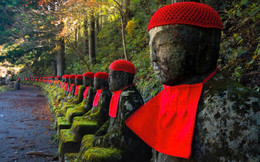 Jizo statues with red hats and bibs along a forest path in Nikko, Japan.