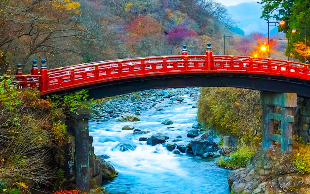 Red Shinkyo Bridge over Daiya River in Nikko, Japan, surrounded by autumn foliage.