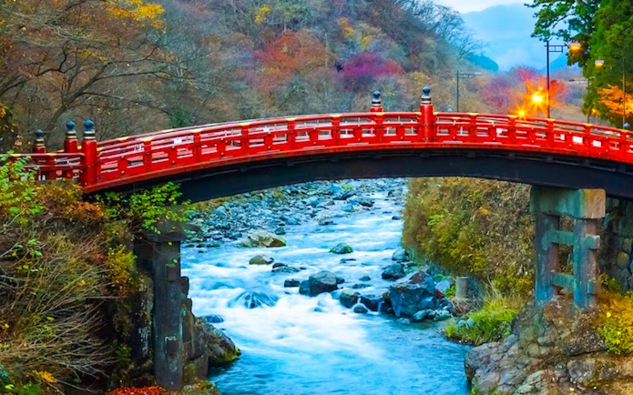 Red Shinkyo Bridge over Daiya River in Nikko, Japan, surrounded by autumn foliage.