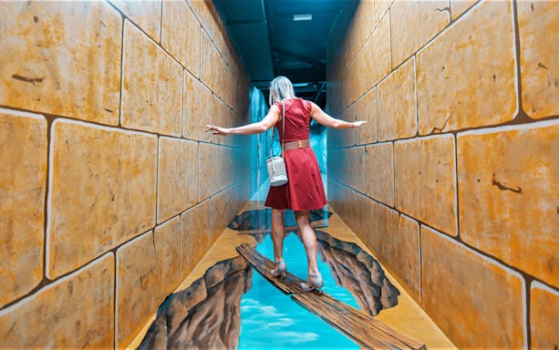 Person balancing on a 3D art bridge illusion at 3D World Dubai Trick-Art Museum.