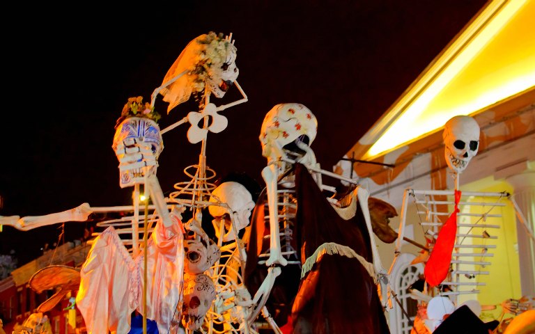 Skeletons in costumes at a Halloween parade viewing party at night.