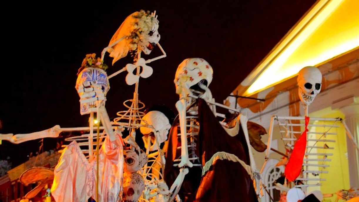 Skeletons in costumes at a Halloween parade viewing party at night.