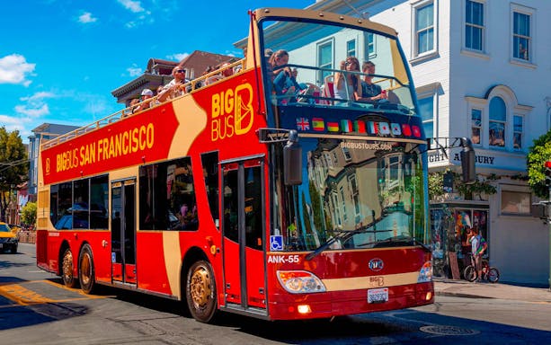Open-top tour bus in San Francisco with passengers exploring city streets.