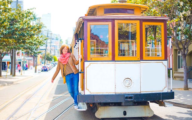 Person riding a San Francisco cable car on a sunny street.