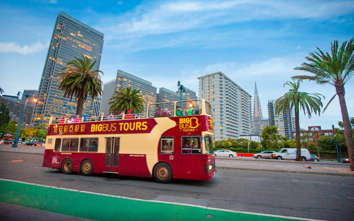 Open-top tour bus in San Francisco with city skyline and palm trees.