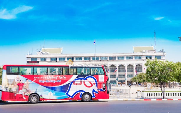 Red double-decker bus for Elephant GOGO Bangkok Hop-On-Hop-Off Tour in front of a government building.