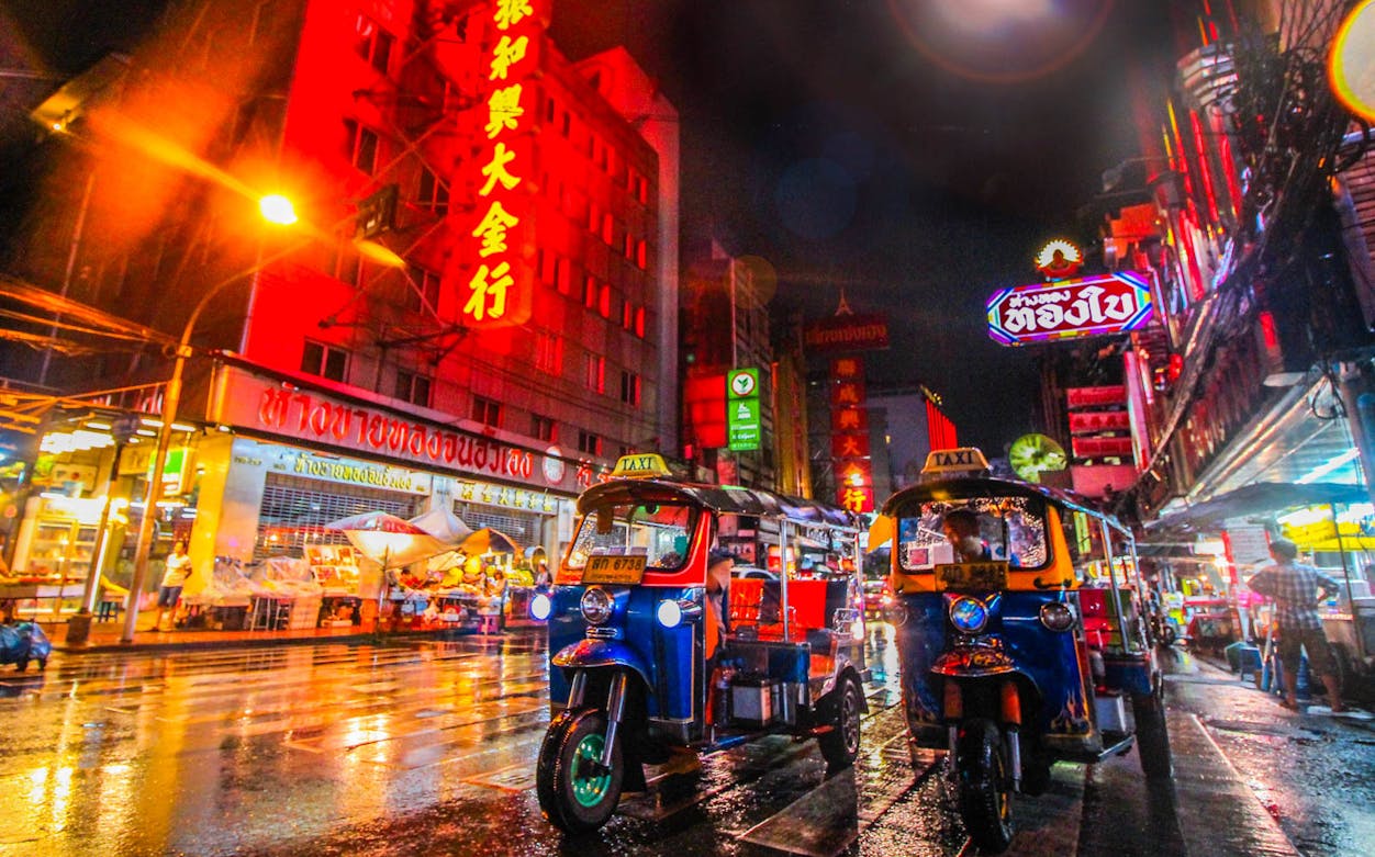 Tuk-tuks on a vibrant street in Bangkok at night during the Giant City Hop-On-Hop-Off Tour.