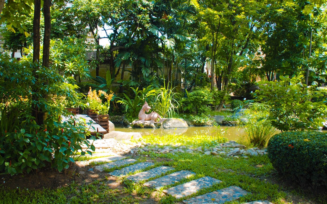 Lush garden with a pond and sculpture at Erawan Museum, Thailand.